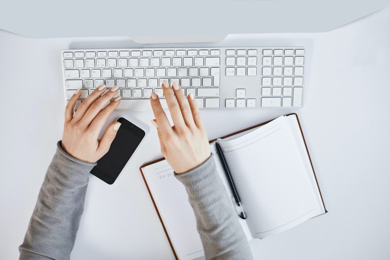 Cropped portrait of woman hands typing on keyboard and working with computer and gadgets. Modern female freelancer designing new project for company, making notes in notebook and smartphone.